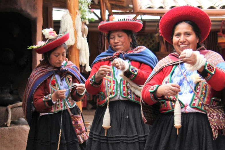 three women in native clothing stand around with hand made items