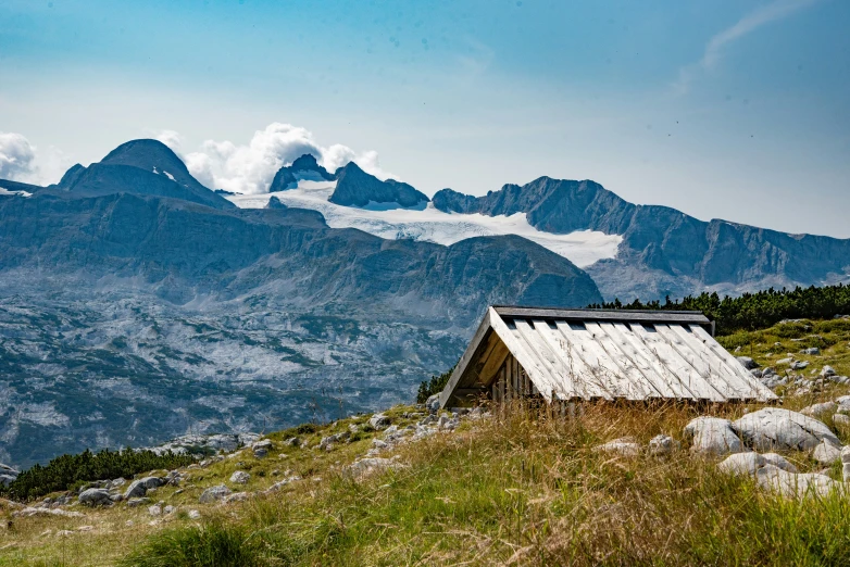 an outhouse on the side of a mountain with clouds in the sky