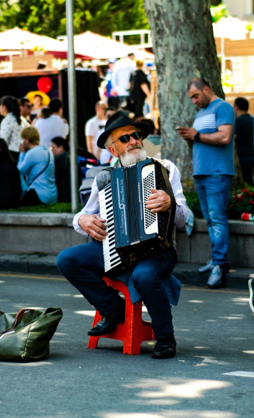 man with a hat holding an accordion while sitting on a bench