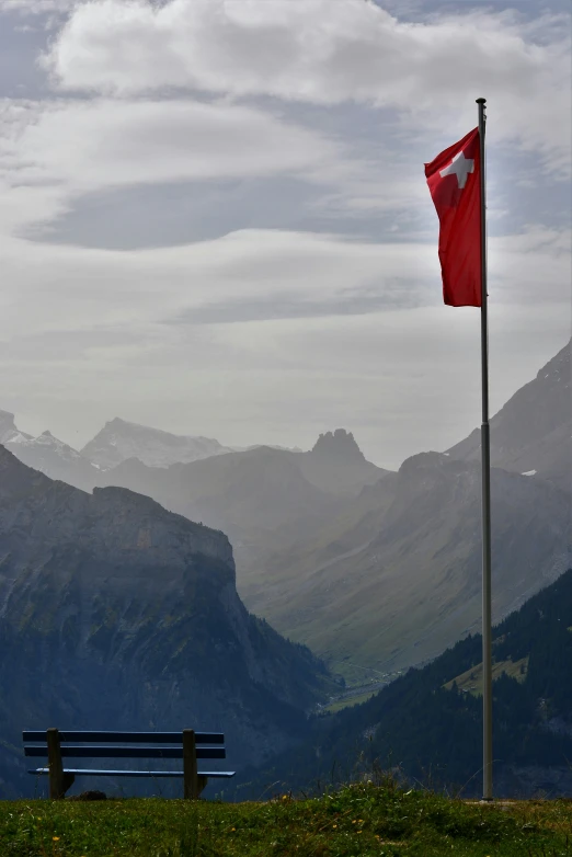 there is a bench with a flag standing in the mountains