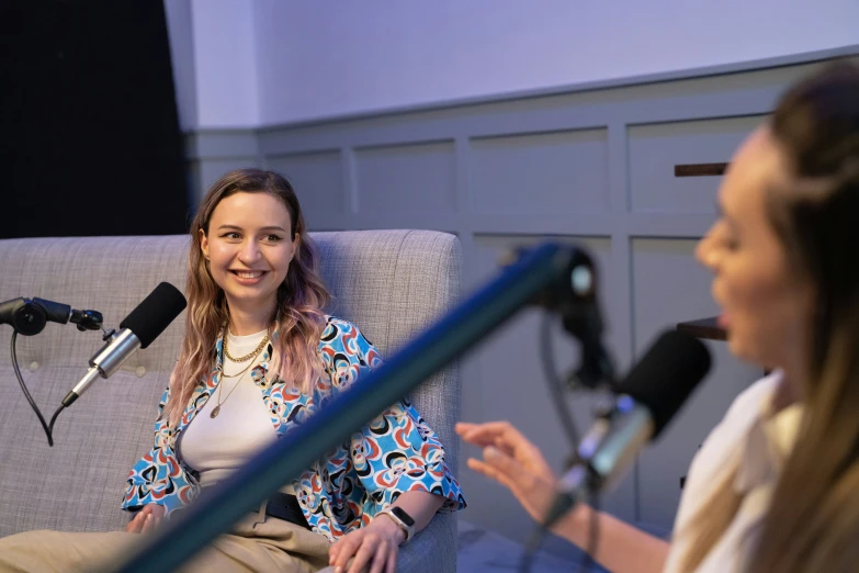 two woman in a gray couch with microphones and lights behind them