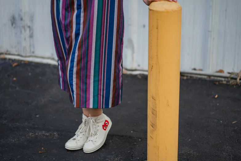 a person standing next to a yellow pole wearing sneakers