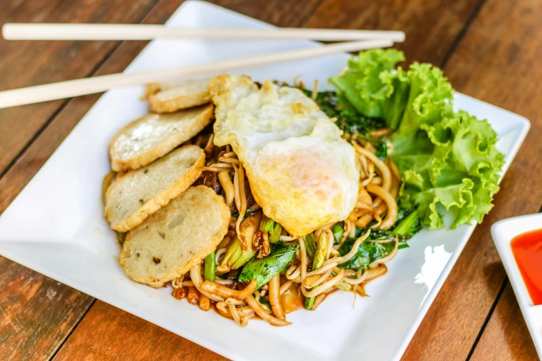 an asian noodle dish with fried egg and rice sticks on a wooden table