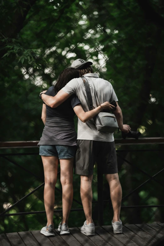 couple on a bridge emcing each other while standing under trees