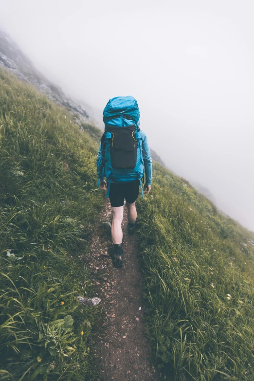 man in blue backpack walking up grassy hill on a foggy day