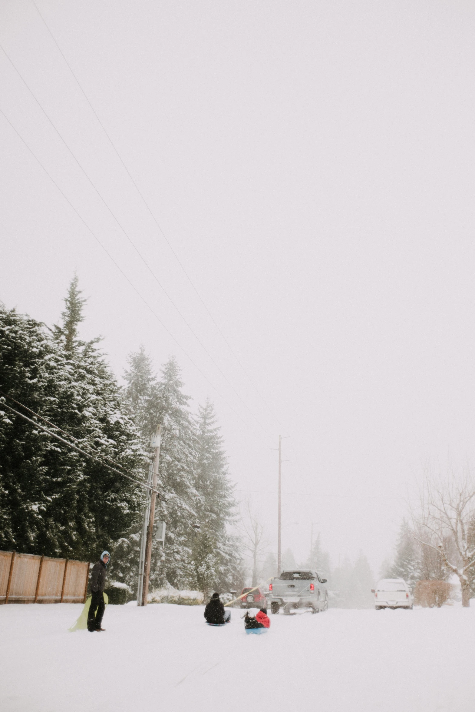 a group of people stand in the snow with a car and some snowboards