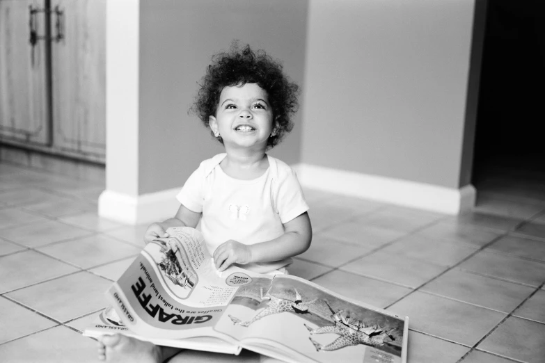 the little girl sits on a floor while reading a book