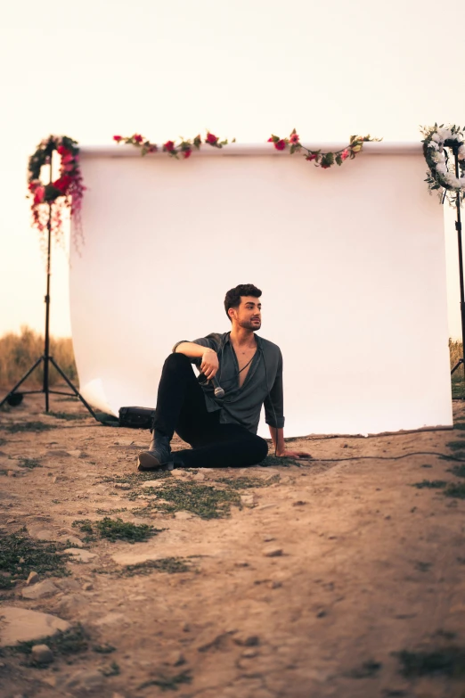 man sitting on the ground next to white backdrop and flowers