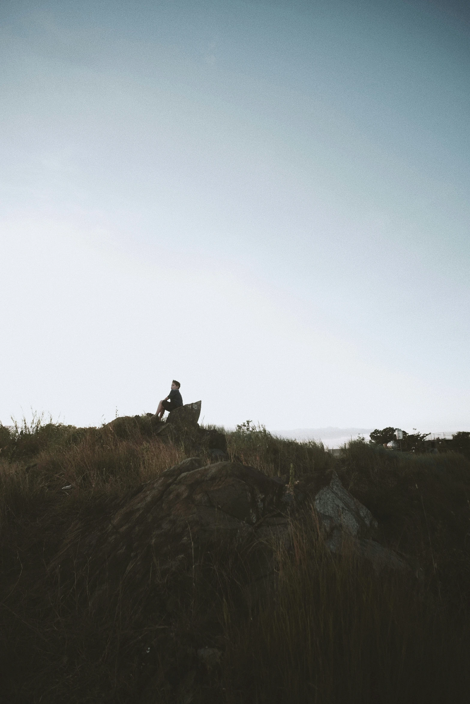 a man sitting on top of a grass covered hill