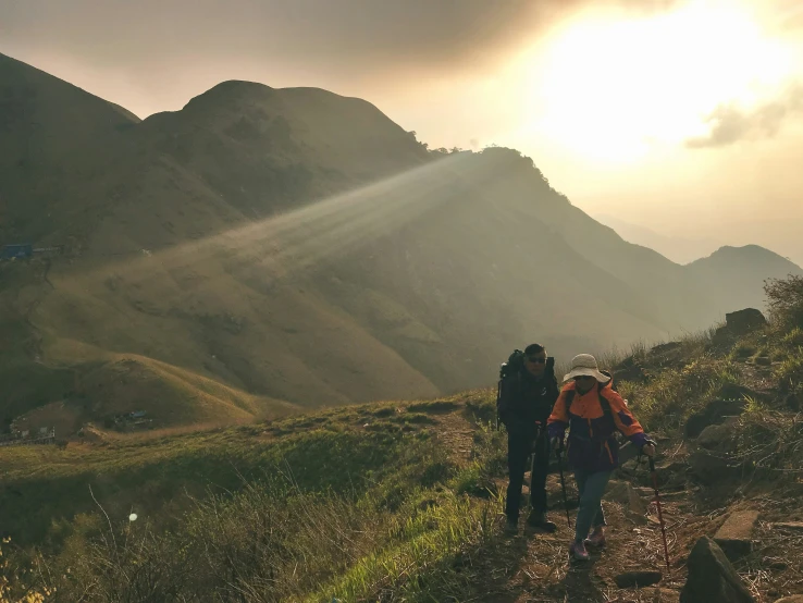 the sun shines down on two people walking up a trail through mountains