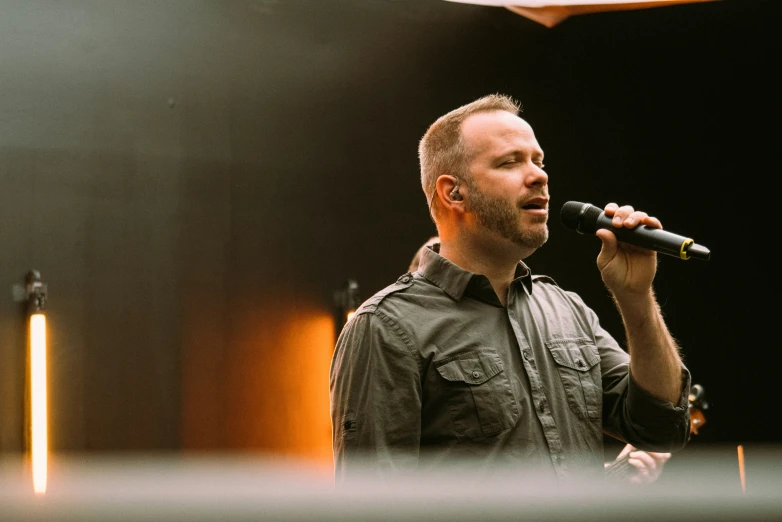 man in black shirt singing into a microphone on stage