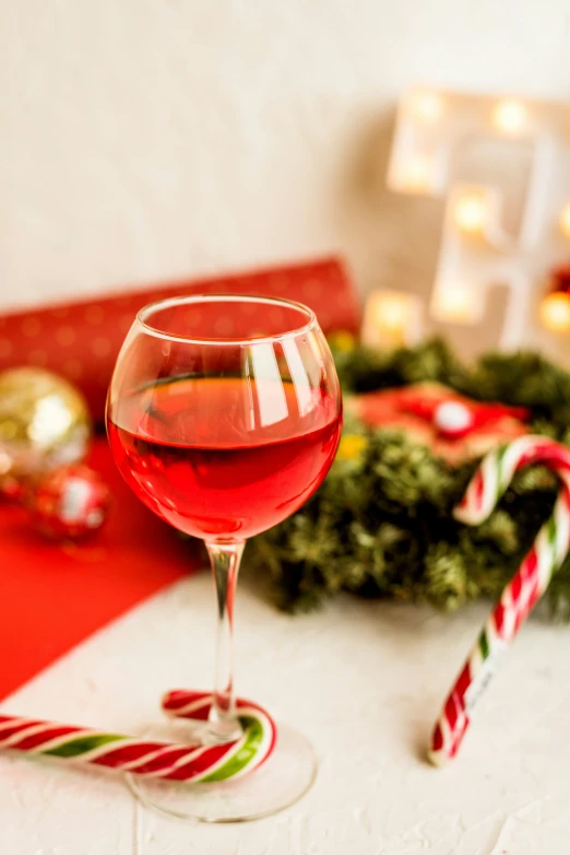 a glass of wine sits next to candy canes and other ornaments