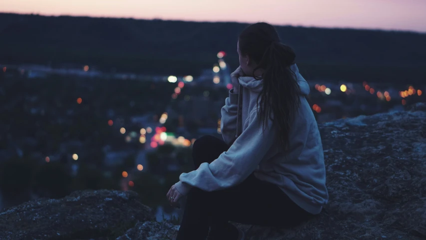 woman sitting alone on a rock overlooking a city