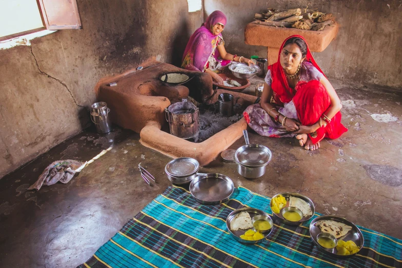 some women sitting around a kitchen stove with food