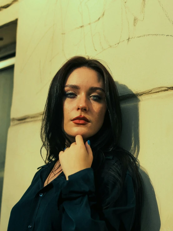 a young woman leans against the wall with her hand under her chin