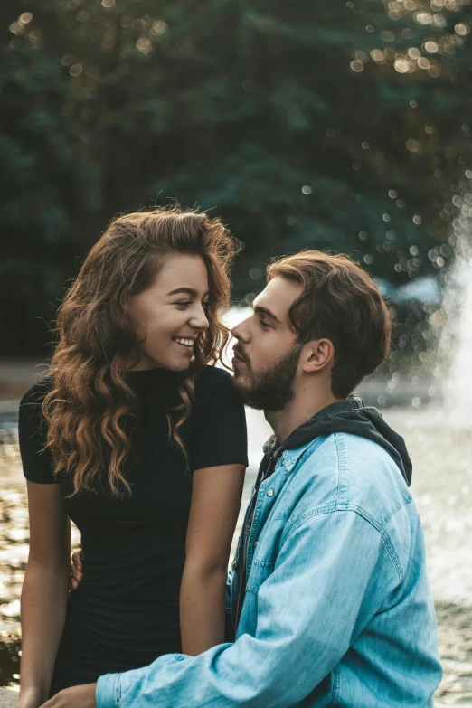 an engaged couple sits next to the water as a fountain