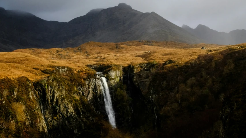 two people walking up a tall waterfall surrounded by mountains