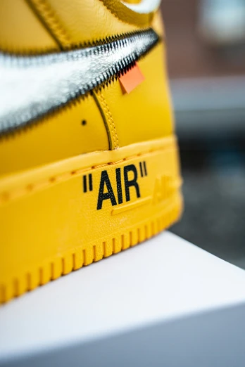 a pair of yellow sneakers has black logo on the soles