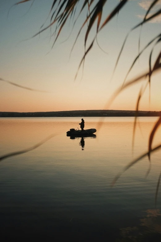 man fishing on calm lake with paddleboat in silhouette