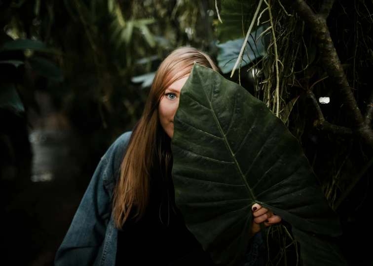 a woman hiding behind leaves in the forest