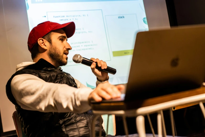 a man at a stage speaking into a microphone while using a laptop computer