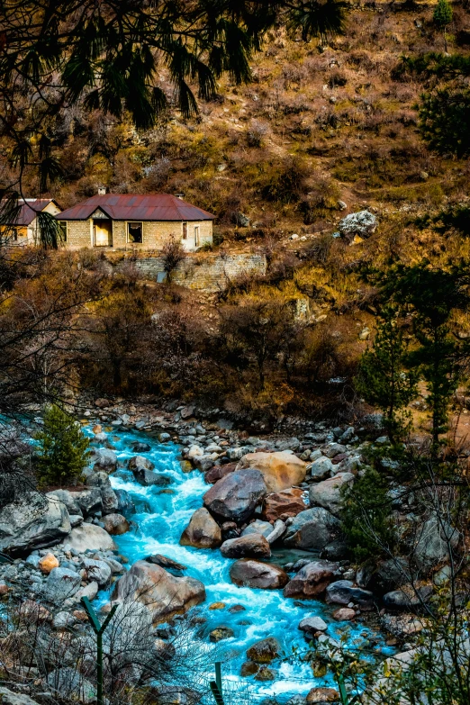 a mountain river is shown in the foreground, with a home on a hillside in the background