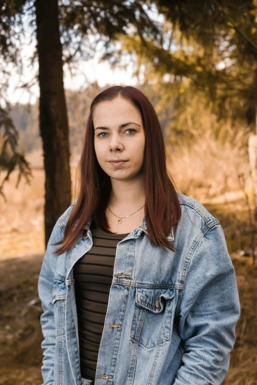 a woman with red hair standing in front of trees