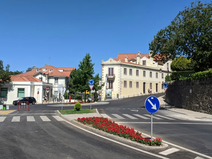 a street with cars parked in front of buildings and flowers and a traffic sign on the corner