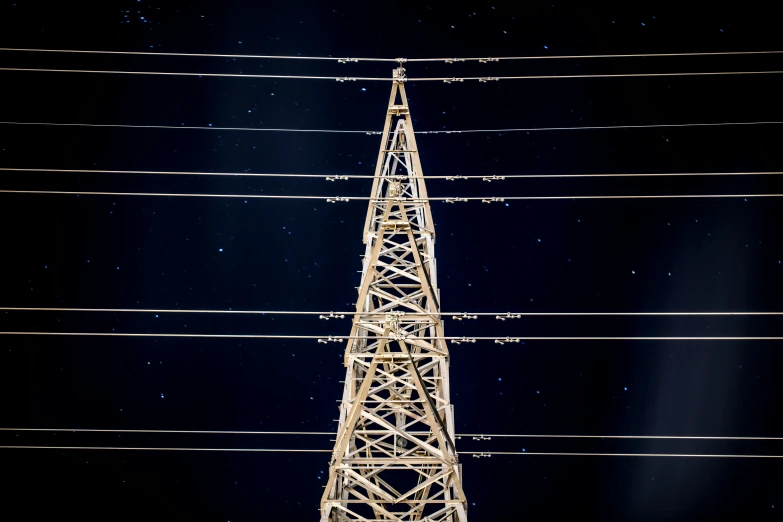 an antenna tower at night with many wires above