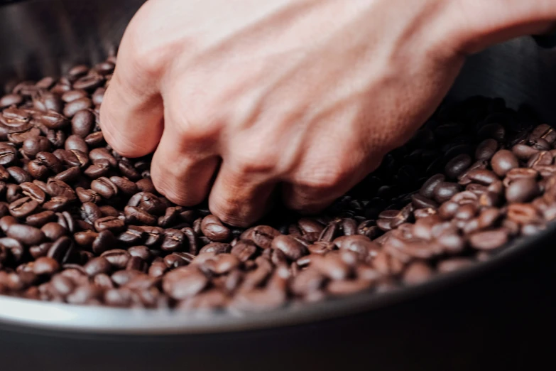 a person grabbing coffee beans into a saucer