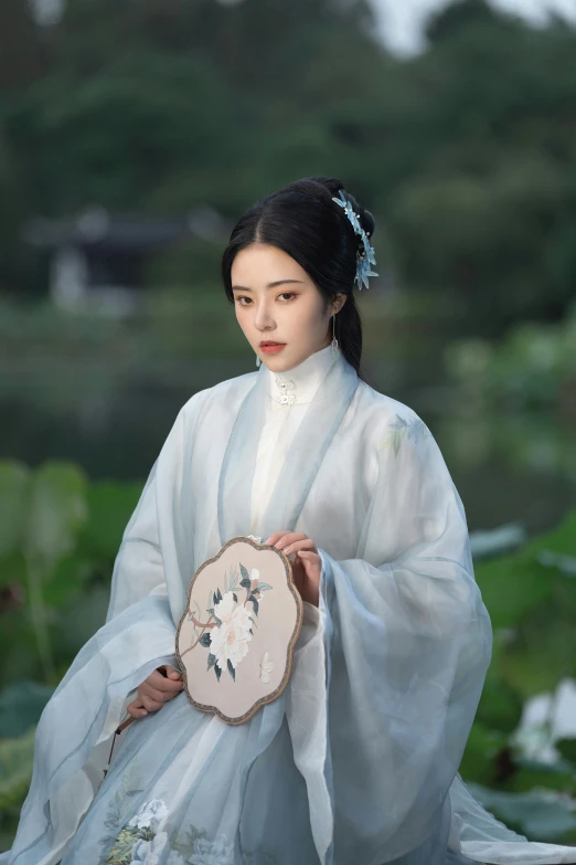 a woman with a frilly standing in the grass holding a fan