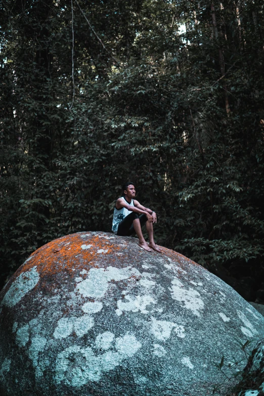 a boy is sitting on the top of a rock