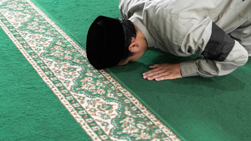 a man wearing a white coat and black hat while kneeling on a rug