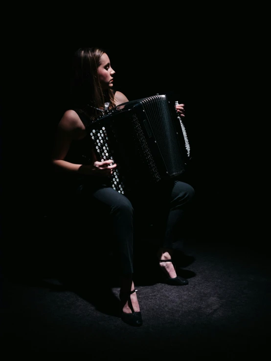 a young woman kneeling with an accordion in the dark