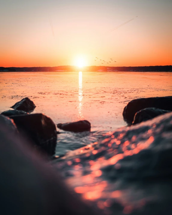 the sun sets over water as the rocks look at them