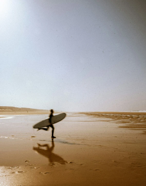 a person walking on top of a beach holding a surfboard