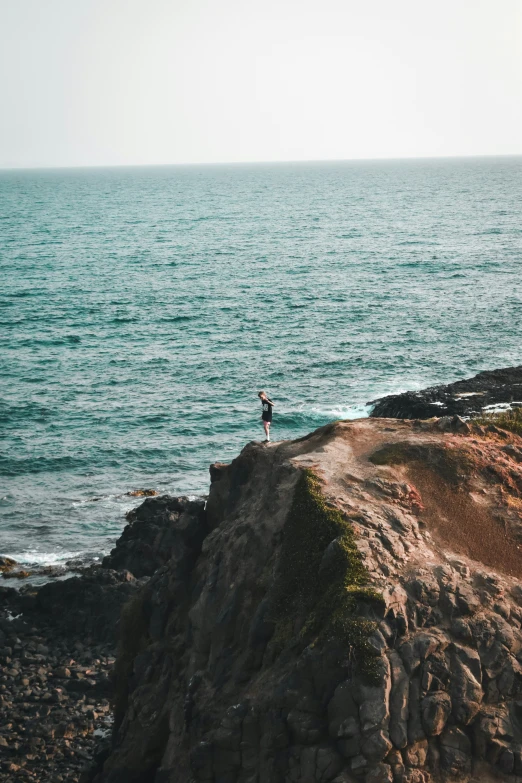 a person on rocks near the ocean and water