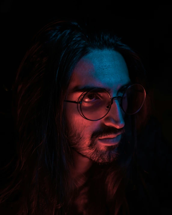 man with long hair and glasses in a dark room