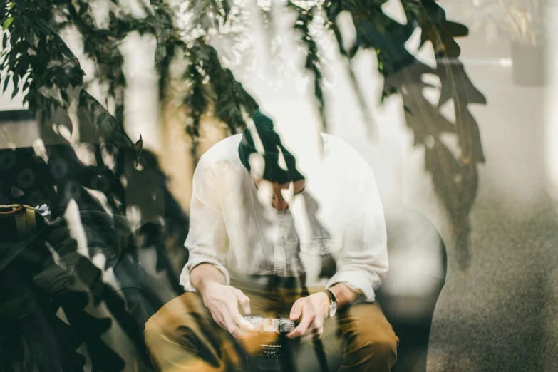 the man is sitting on the couch in front of the plant