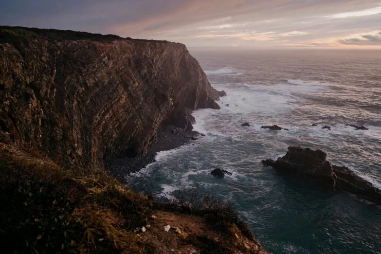 a cliff is overlooking the ocean while clouds are in the sky