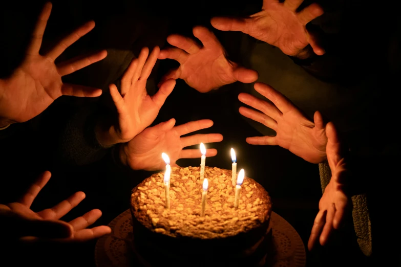 many hands reaching for a cake with several lit candles