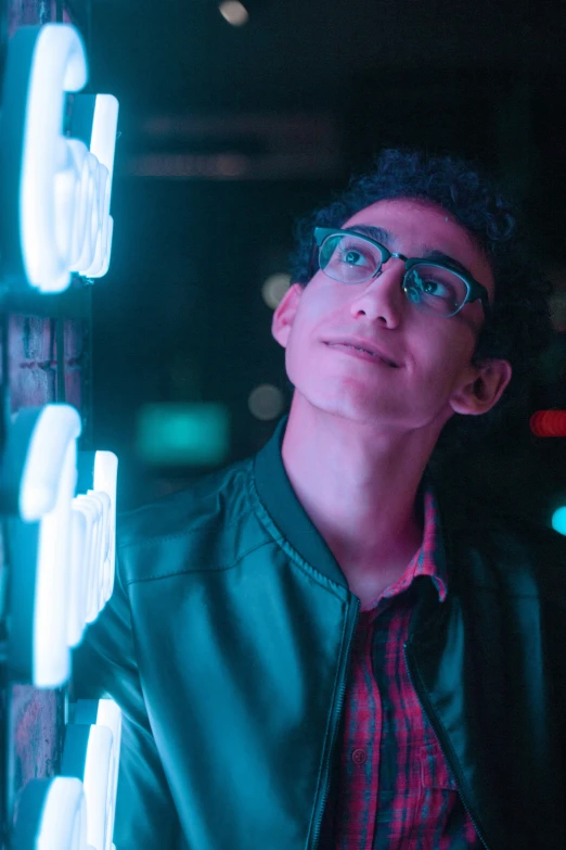 a man in glasses poses in front of neon light