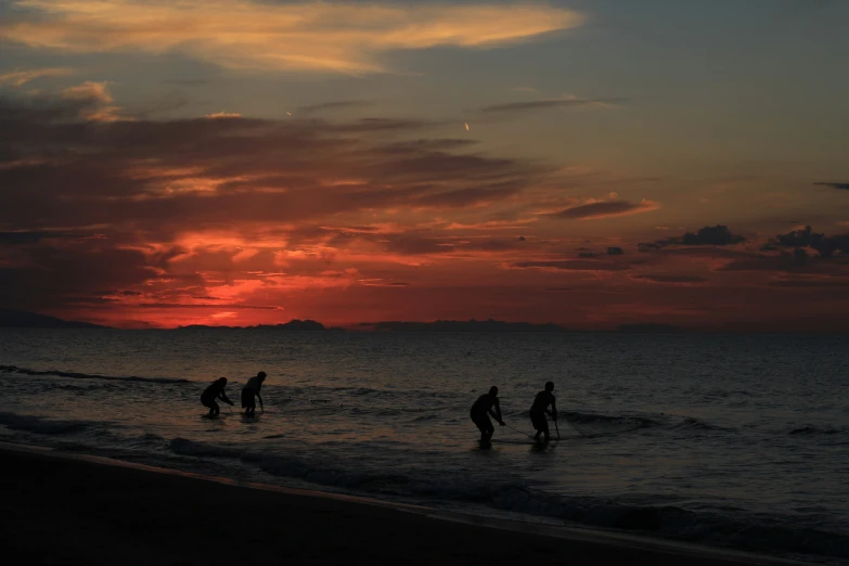 people stand on the beach at dusk with the setting sun