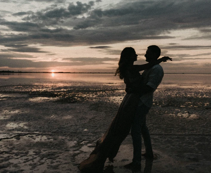 a couple standing next to each other on a beach under a cloudy sky