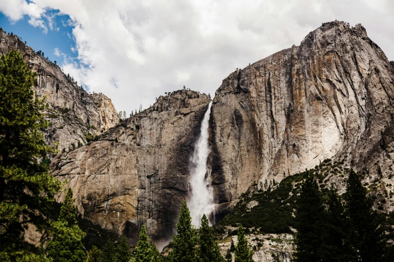 a tall waterfall cascades into the sky with some trees around it