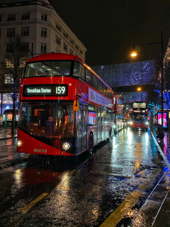 a couple of double decker buses are going down the street at night