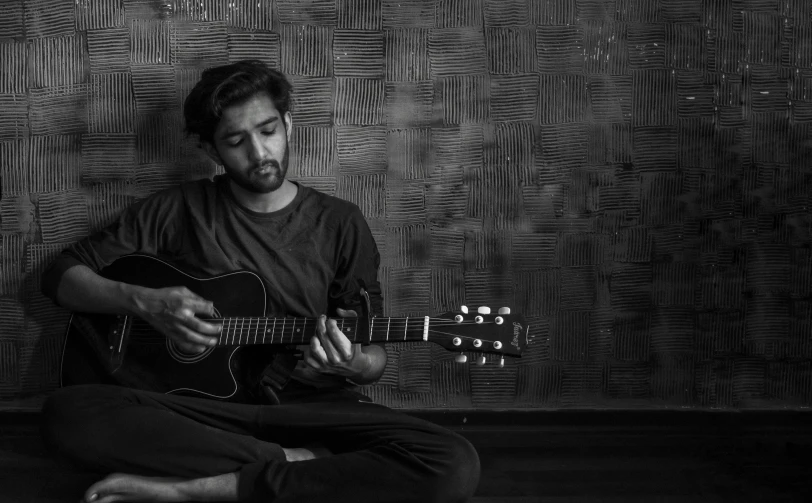 man sitting on floor playing guitar in front of wallpaper