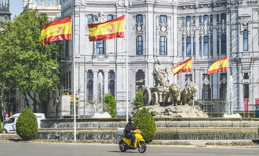 yellow scooter with spanish flags parked in front of large buildings