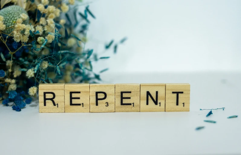 a wooden block that reads repent near some flowers