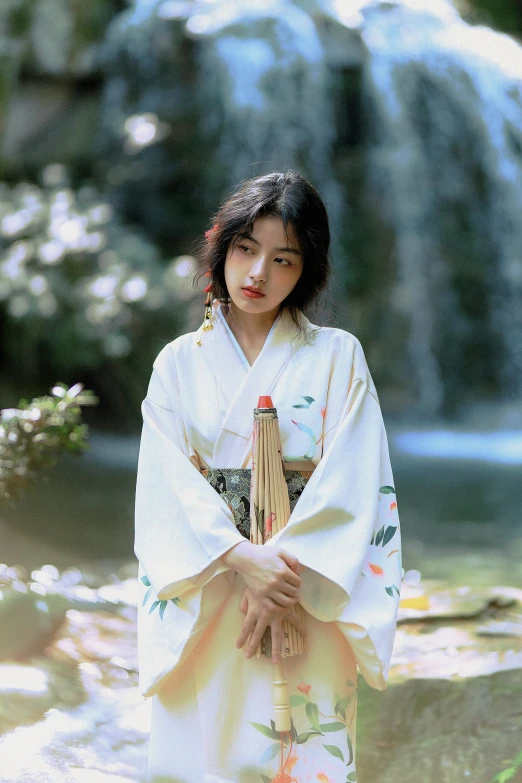 woman dressed in traditional geisha dress with japanese style clothing standing near a waterfall